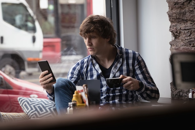 コーヒーを飲みながら携帯電話を使用している男性