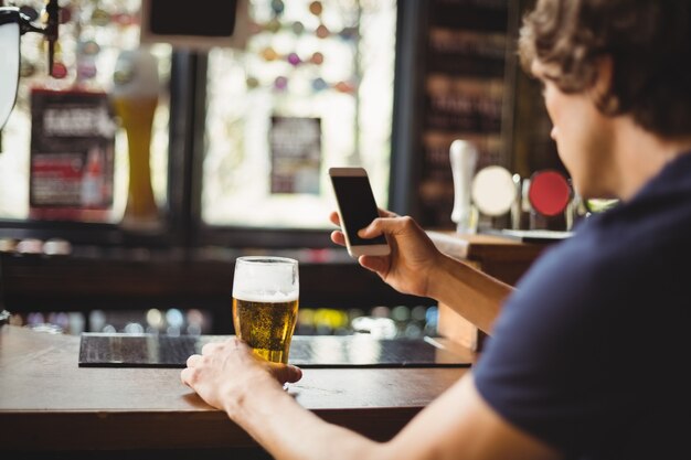 Man using mobile phone with glass of beer in hand