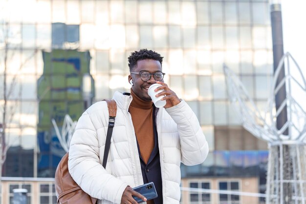 Мужчина с помощью телефона с беспроводными наушниками гуляет по городу и пьет кофе