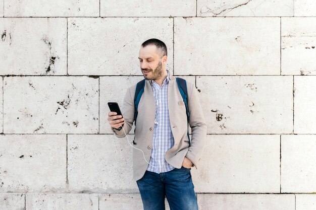 無料写真 石の壁の近くにスマートフォンを使用している男