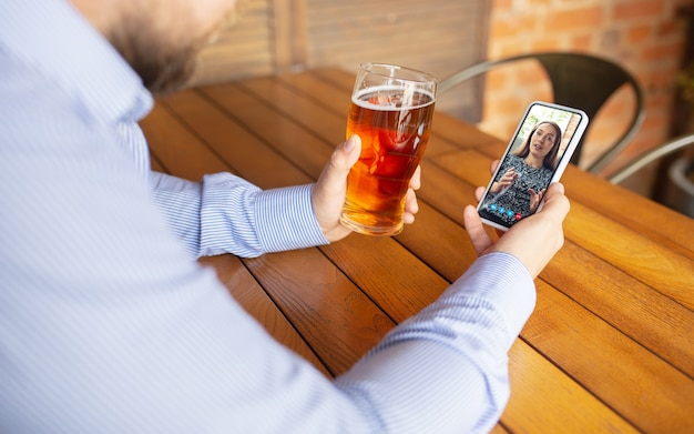 Foto gratuita uomo che utilizza smartphone per la videochiamata mentre beve una birra