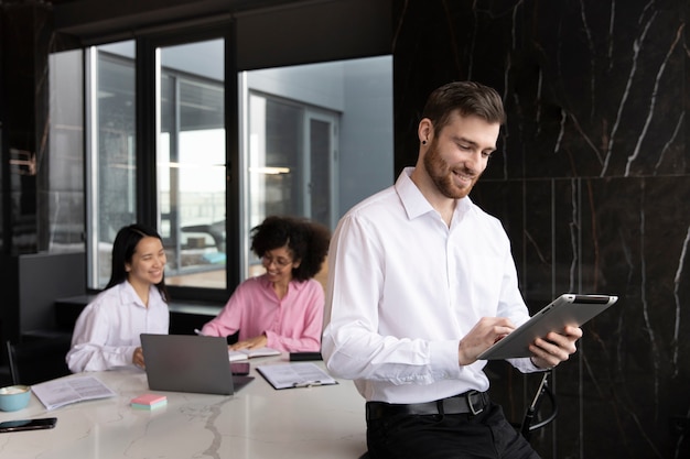 Man using a tablet to work while his female colleagues are using a laptop