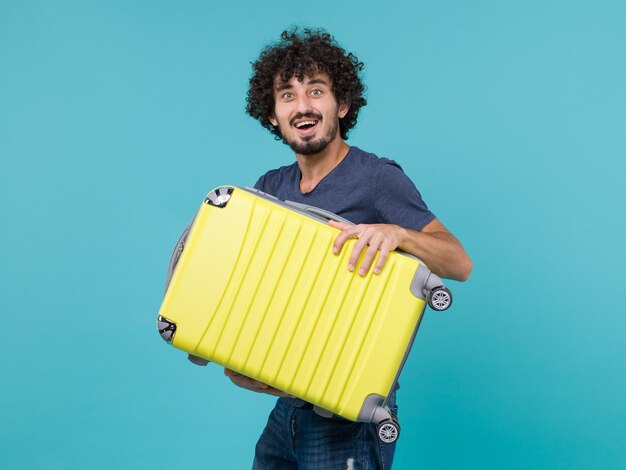 man in vacation holding big yellow suitcase on blue