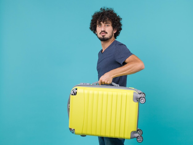 man in vacation holding big yellow suitcase on blue