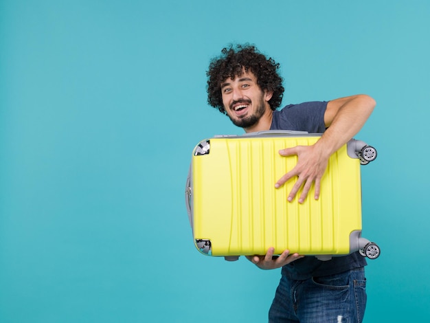 man in vacation holding big yellow suitcase laughing on blue