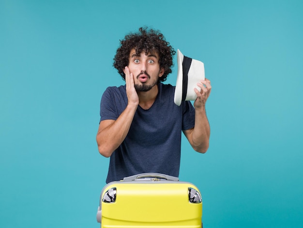 Foto gratuita uomo in vacanza che tiene il cappello su azzurro