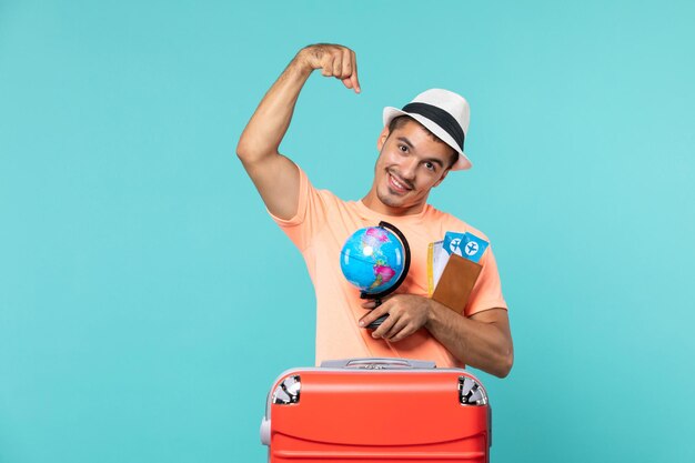 man in vacation holding little globe and tickets on light blue