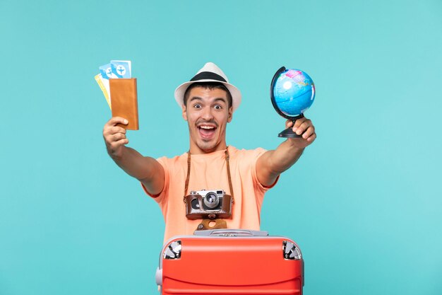 человек в отпуске держит маленький глобус и билеты на голубом