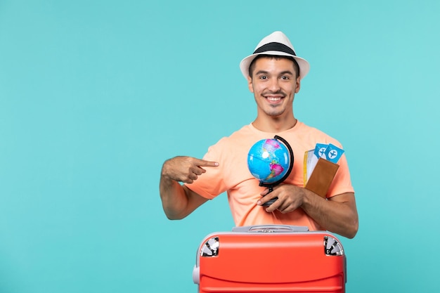 man in vacation holding little globe and tickets smiling on blue