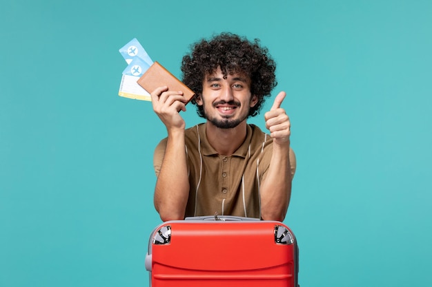 Man in vacation holding tickets on light-blue