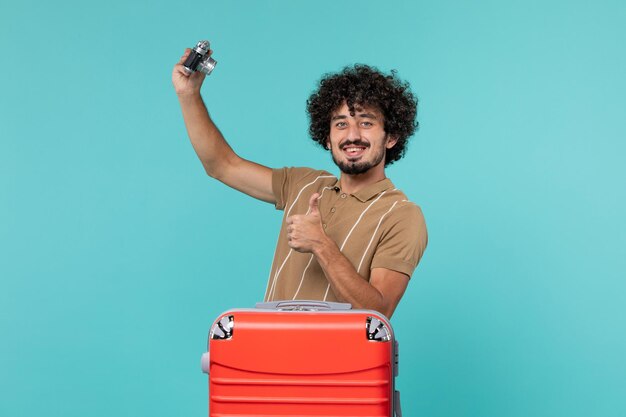 man in vacation with big red suitcase taking photos with camera on blue