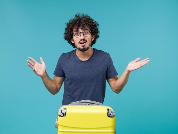 man in vacation with his big yellow suitcase on light blue