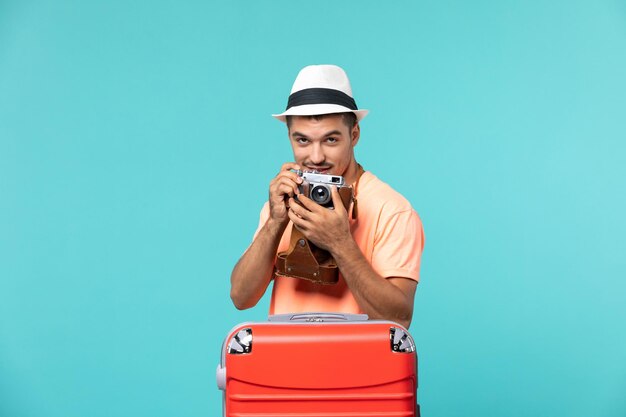 休暇中の男が赤いスーツケースを持ち、青のカメラで写真を撮る