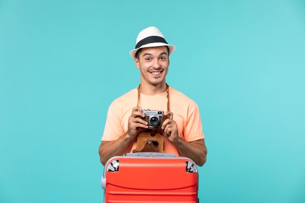 man in vacation with his red suitcase taking photos with camera on blue