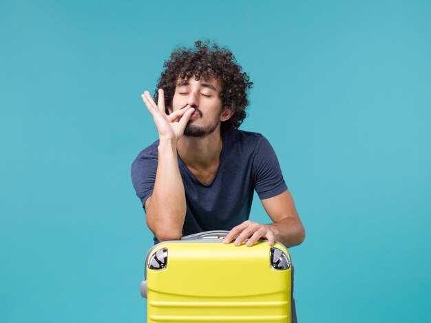 man in vacation with his yellow suitcase on light blue