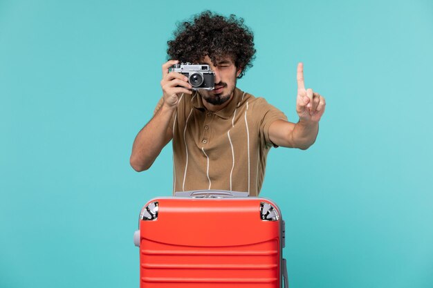青い床の旅でカメラで写真を撮る赤いスーツケースを持った休暇中の男 飛行機の休暇 海の航海旅行