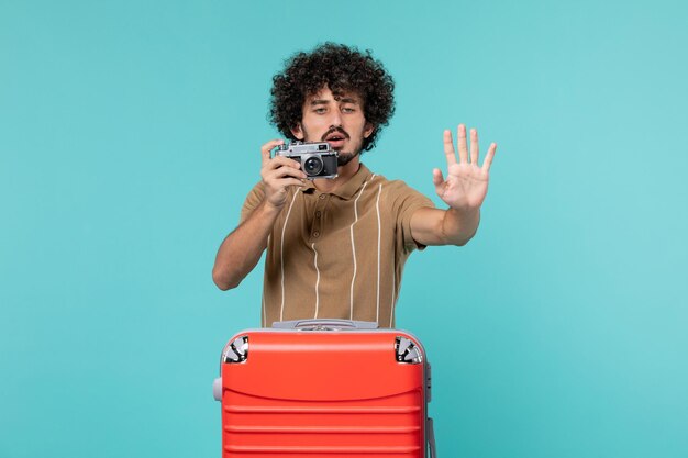 man in vacation with red suitcase taking photos with camera on blue