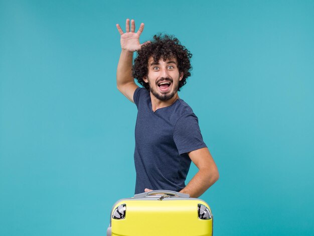 man in vacation with yellow suitcase feeling happy on blue