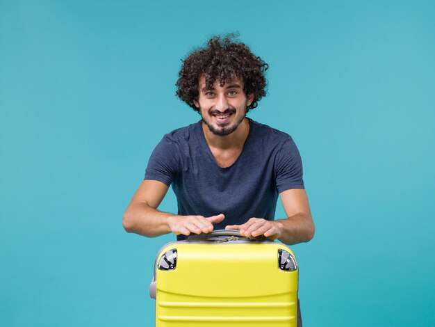青に幸せな気分で黄色のスーツケースを持つ休暇中の男
