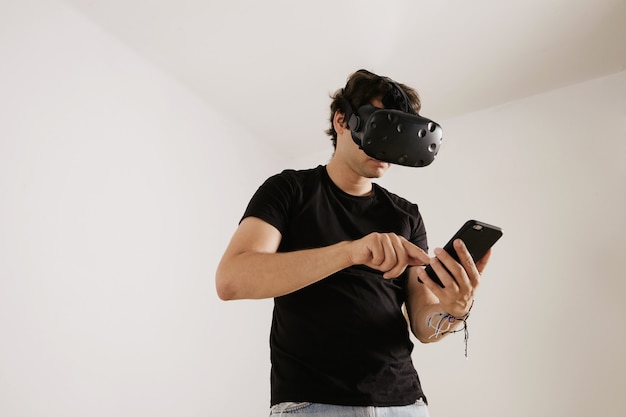 A man in VR glasses and black unlabeled t-shirt swiping on his smartphone's screen on white