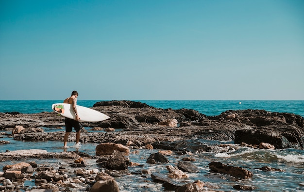 Man walking on sea shore with surfboard 