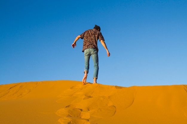 Free photo man walking on top of dune in desert