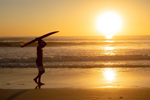 해변에서 그의 머리에 서핑 보드와 함께 걷는 남자