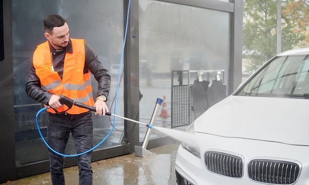 Foto gratuita uomo che lava l'auto sulla stazione di autolavaggio che indossa un giubbotto arancione