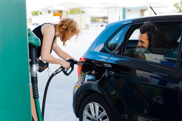 Man watching out of car window how woman filling up car 
