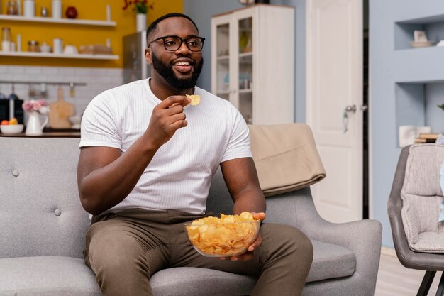 Человек смотрит телевизор и ест чипсы