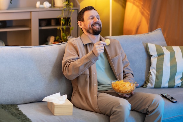 テレビを見たり、チップを食べたりする男