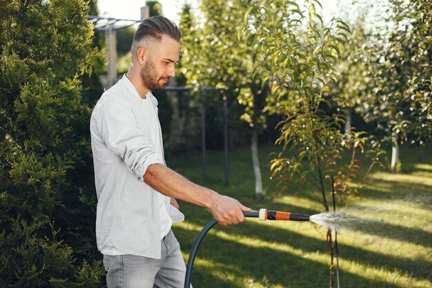 Мужчина поливает растения в своем саду. Мужчина в голубой рубашке.