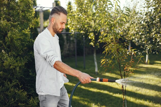 彼の庭で彼の植物に水をまく男。青いシャツを着た男。