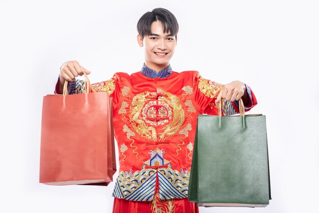 Мужчина в костюме Cheongsam улыбается с бумажным пакетом после покупок в китайском новом году
