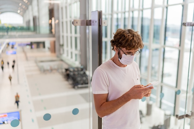 Foto gratuita uomo che indossa la maschera per il viso in aeroporto e utilizza lo smartphone