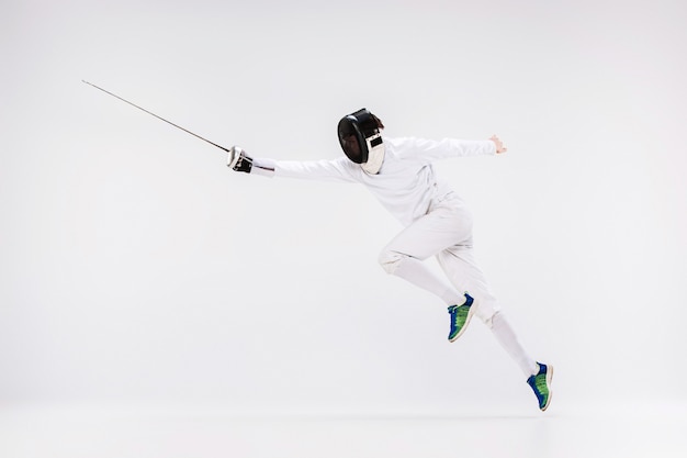 Man wearing fencing suit practicing with sword against gray