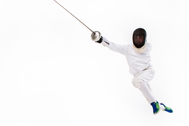 Man wearing fencing suit practicing with sword against gray