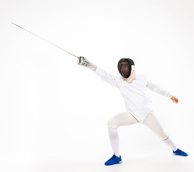 Man wearing fencing suit practicing with sword against gray