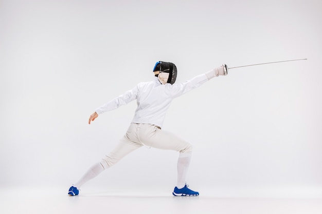 Free photo man wearing fencing suit practicing with sword against gray