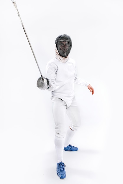 Man wearing fencing suit practicing with sword against gray