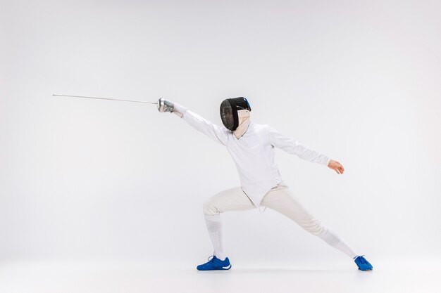 Man wearing fencing suit practicing with sword against gray