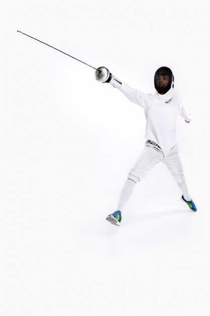 Man wearing fencing suit practicing with sword against gray