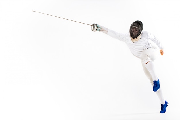 Man wearing fencing suit practicing with sword against gray