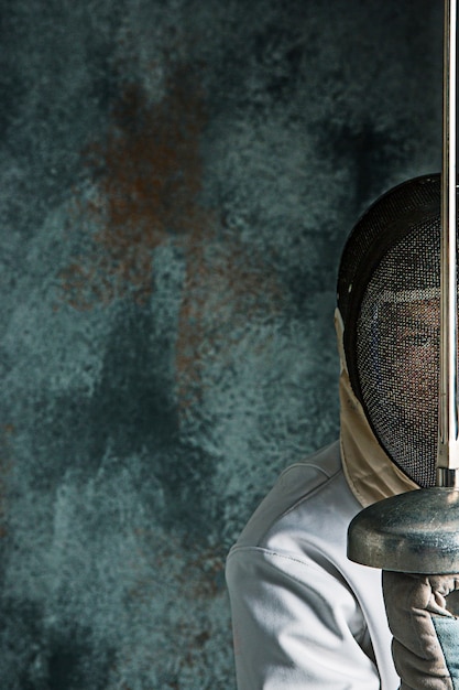 Free photo the man wearing fencing suit with sword against gray