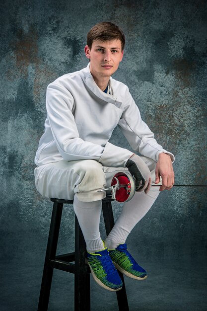 The man wearing fencing suit with sword against gray