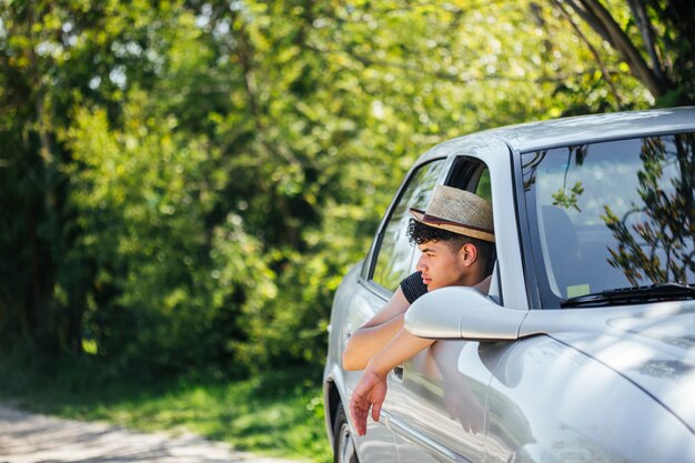 Шляпа человека нося смотря природу через окно автомобиля