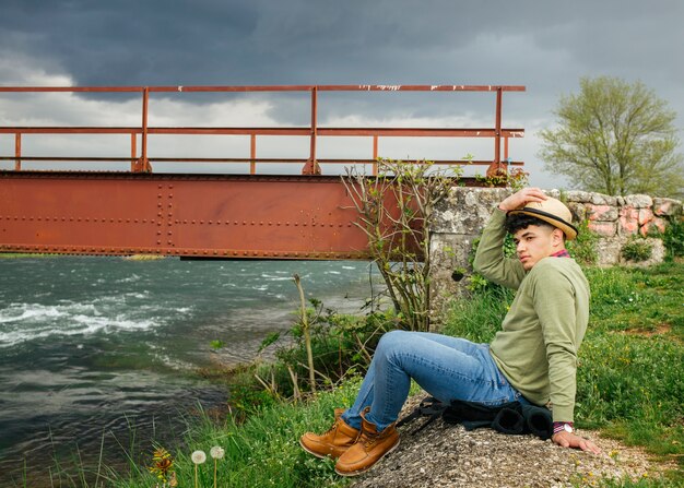 Man wearing hat sitting near flower river