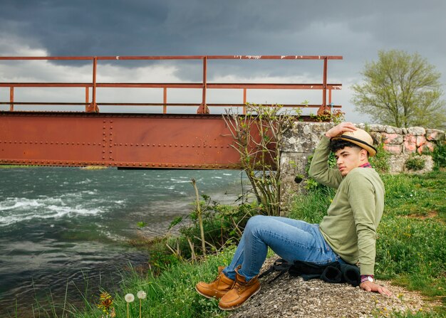 Человек в шляпе сидит возле реки цветок