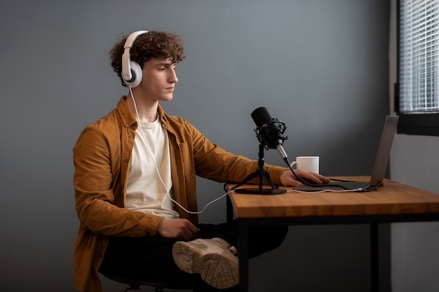 A podcaster recording in a professional studio with a microphone, headphones, and a laptop, surrounded by sponsorship logos