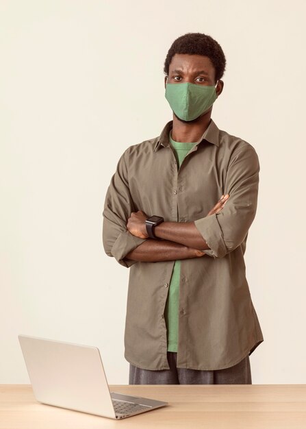 Man wearing medical mask standing next to his laptop